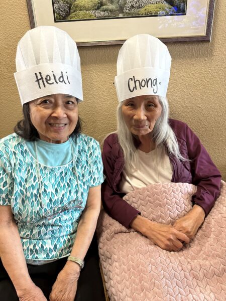 two elderly women wearing chef hats during a life enrichment activity called cooking club 